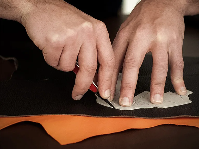Un artigiano mentre taglia la pelle prima del montaggio della scarpine primi passi Barberini, totalmente Made in Italy